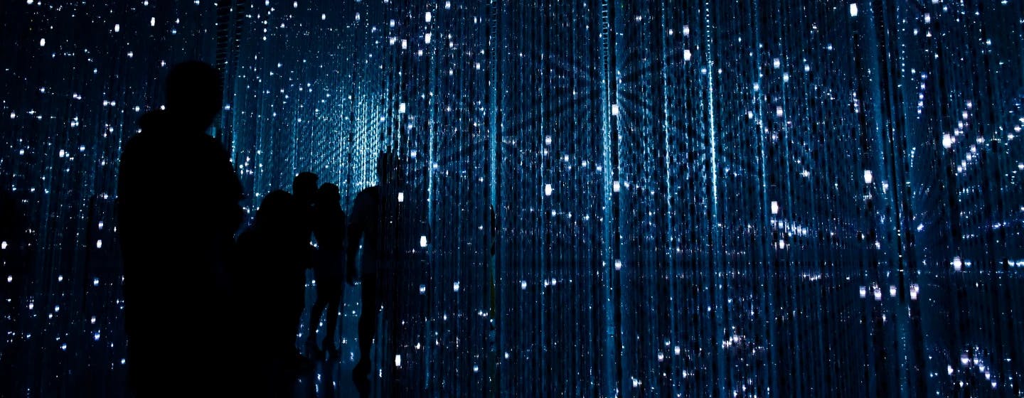 people in silhouette in a room of star-like lights, representing the future